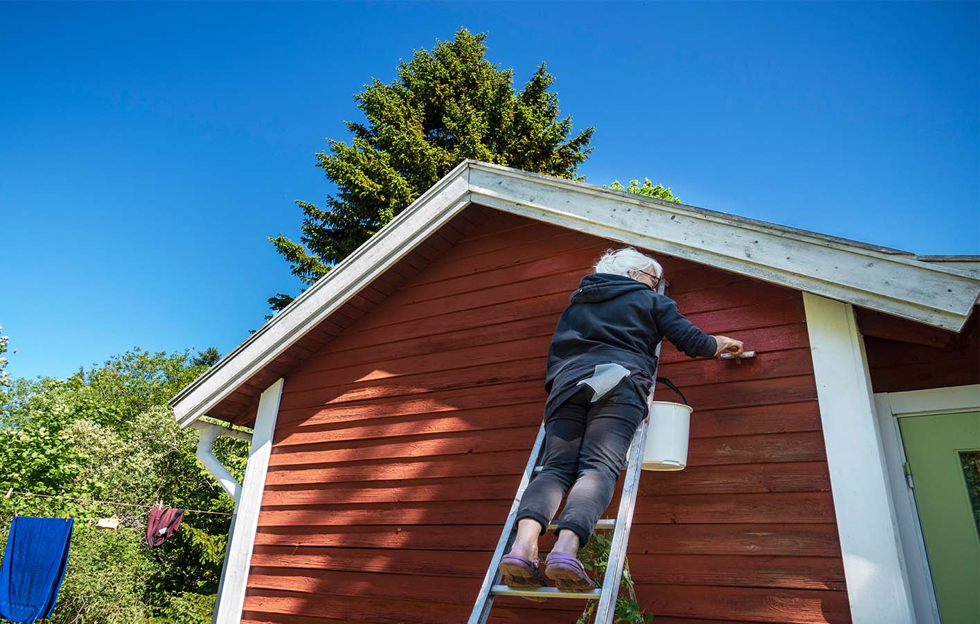 Eine Frau streicht eine Holzfassade im typischen Schwedenrot